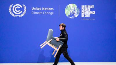 Ein Mitarbeiter trägt bei der UN-Klimakonferenz COP26 einen Stuhl von einer Bühne.