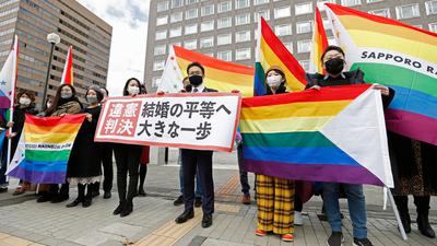 Anwälte der Kläger und Unterstützer halten 2021 Regenbogenflaggen und ein Transparent mit der Aufschrift: „Verfassungswidriges Urteil“ vor dem Bezirksgericht Sapporo hoch.