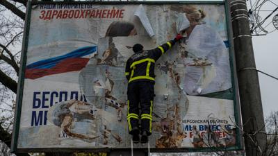 Ein ukrainischer Feuerwehrmann reißt in der kürzlich befreiten Stadt Cherson eine russisches Werbeplakat von einer Werbetafel.