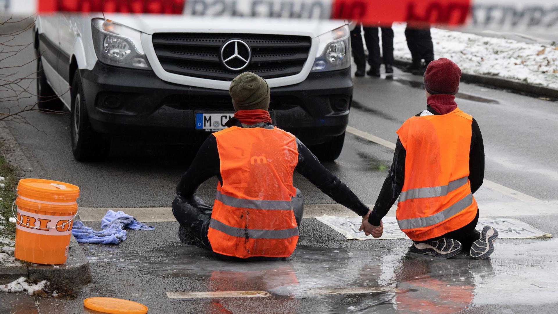 Zwei Klimaaktivisten der „Letzten Generation“ versuchen, sich auf einer Straße in München trotz Nieselregen und Minusgraden festzukleben.