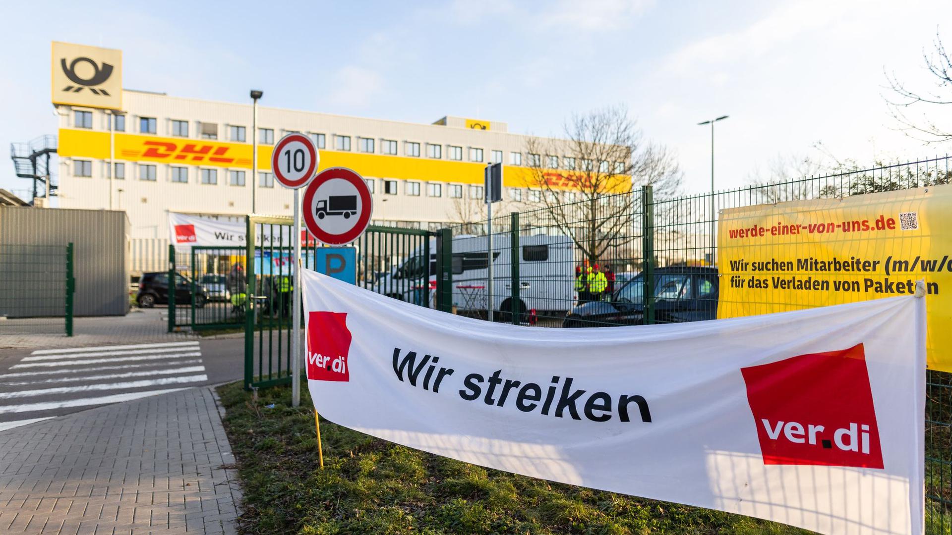 Ein Banner mit der Aufschrift „Wir streiken“ hängt vor einem Gebäude des Paketdienstleisters DHL in Lahn.
