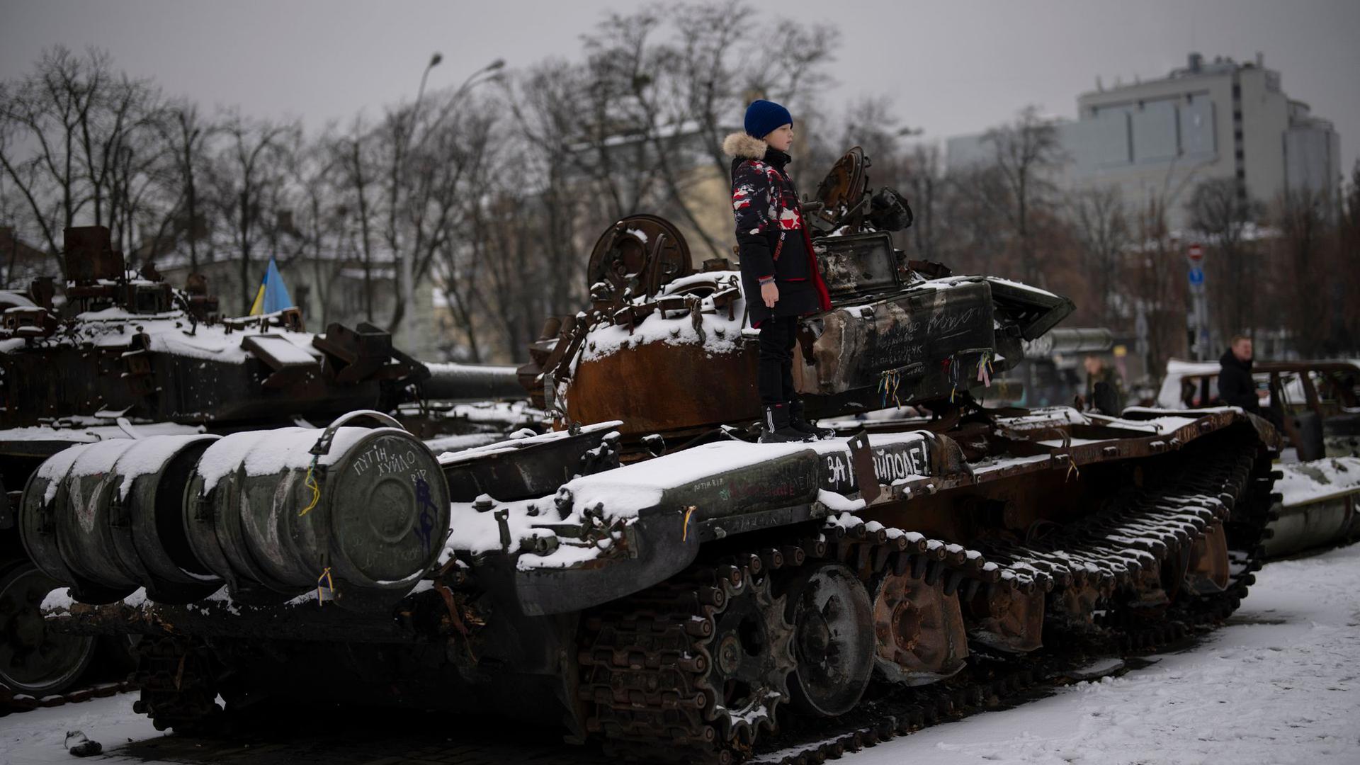 Ein Junge steht auf einem zerstörten russischen Panzer in der Kiewer Innenstadt.