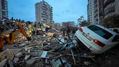 Notfallteams suchen nach Menschen in einem zerstörten Gebäude, während ein Auto auf den Trümmern liegt. Nach mehreren schweren Erdbeben in der türkisch-syrischen Grenzregion ist die Zahl der Toten auf mehr als 1900 gestiegen.