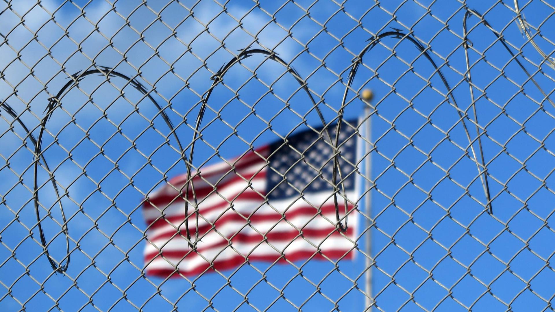 Eine US-Flagge hinter Zaun und Stacheldraht auf dem Marinestützpunkt Guantánamo Bay auf Kuba. Hier betreiben die USA seit mehr als 21 Jahren ein umstrittenes Gefangenenlager.