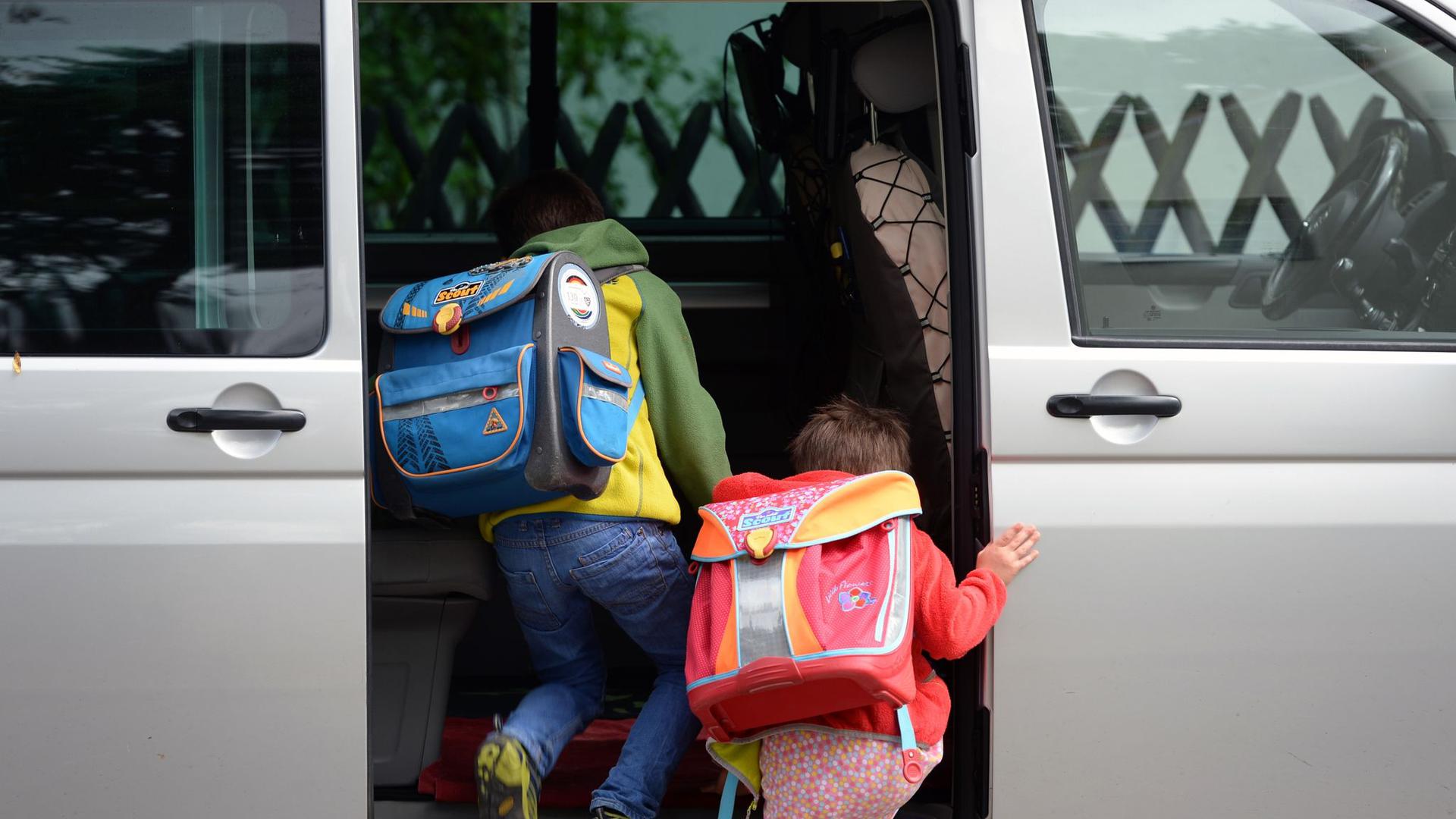 Zwei Kinder mit Schulranzen steigen in ein Auto ein. 