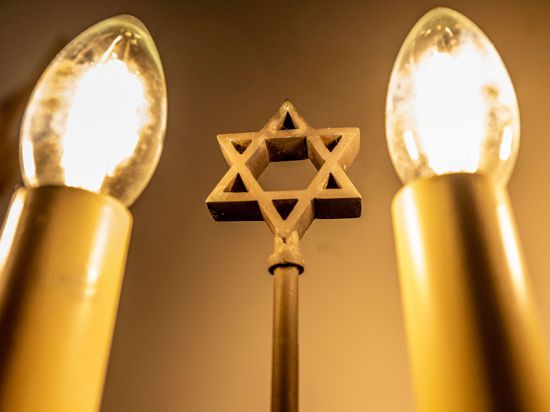 Ein siebenarmiger Leuchter (Menora) mit einem Davidstern in der Mitte leuchtet in einer Synagoge. Fragen zum Judentum werden auf einer Website beantwortet.