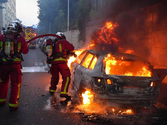 Feuerwehrleute löschen am Rande von Ausschreitungen westlich von Paris ein brennendes Auto.