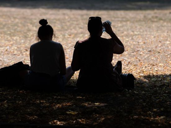Zwei Frauen sitzen in einem Park im Schatten der Bäume, um sich vor der Hitze zu schützen.
