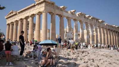 Touristen unter einem Sonnenschirm vor der Akropolis, die inzwischen geschlossen wurde.