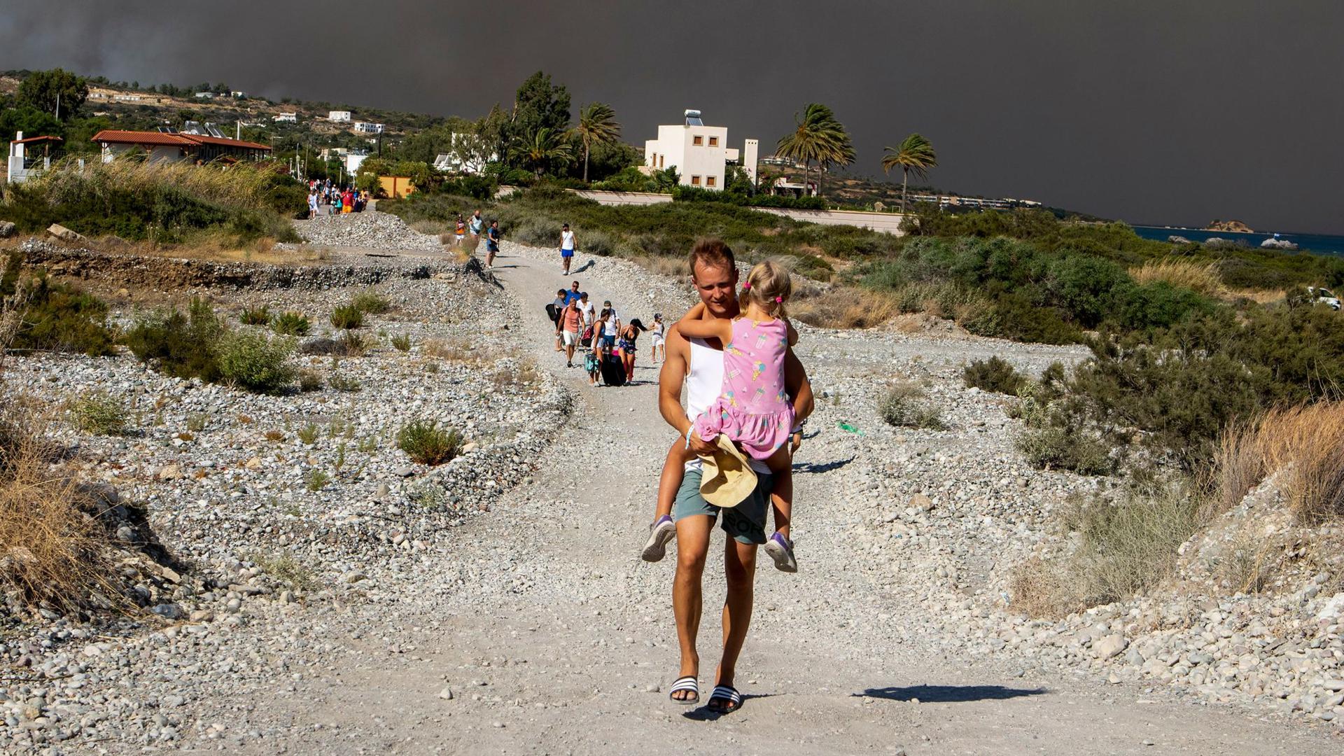 Menschen verlassen ein Waldbrandgebiet auf Rhodos. Auf der griechischen Insel wüten weiter mehrere Brände.