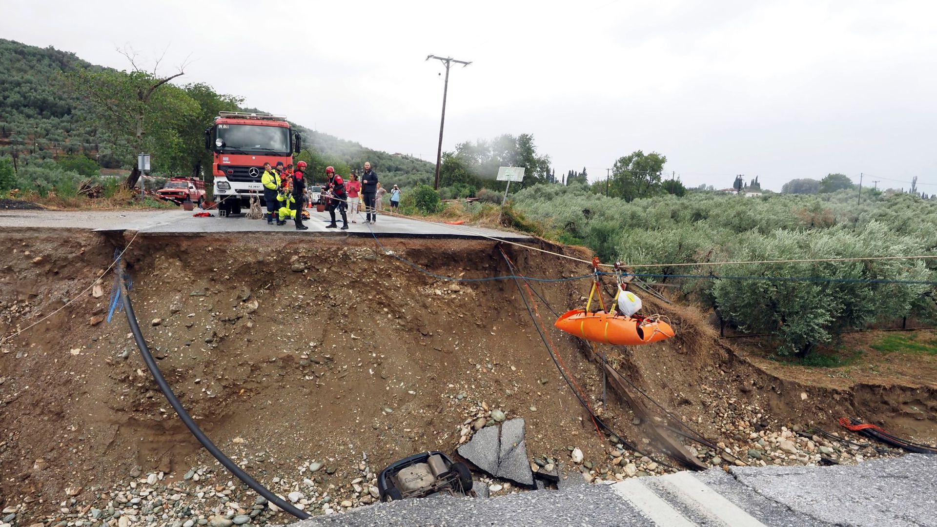 Feuerwehrleute heben im griechischen Kala Nera einen Nierenpatienten über eine durch einen Regensturm beschädigte Straße.