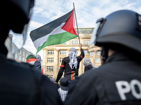 Ein Teilnehmer einer verbotenen Pro-Palästina-Demonstration in Frankfurt am Main schwenkt eine Palästina-Flagge, während Polizisten die Situation beobachten.