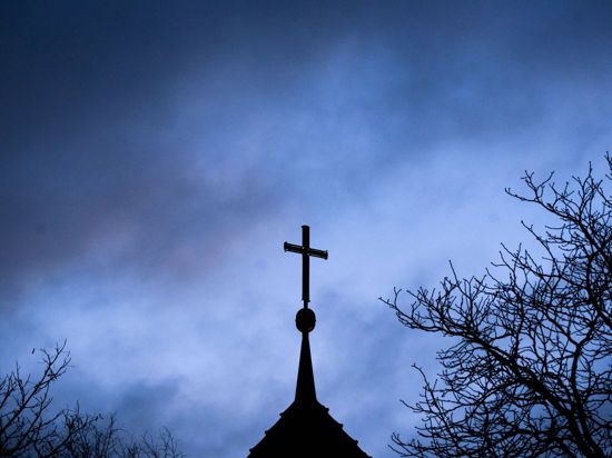 Dunkle Wolken über einem Kreuz einer Kirche: Einem der Missbrauchsopfer muss Schadenersatz gezahlt werden (Symbolbild).