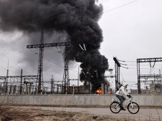 Nach einem russischen Angriff fährt ein Mann mit seinem Rad an einem brennenden Elektrizitätswerk in Charkiw vorbei.