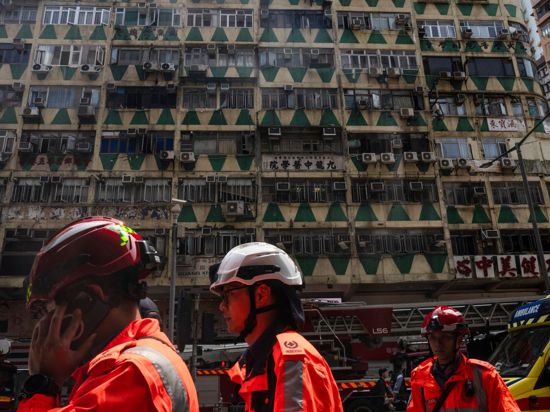 Im Hintergrund ist das ausgebrannte Hochhaus in Hongkong zu sehen – bei der Feuerwehr waren zahlreiche Hilferufe eingegangen.
