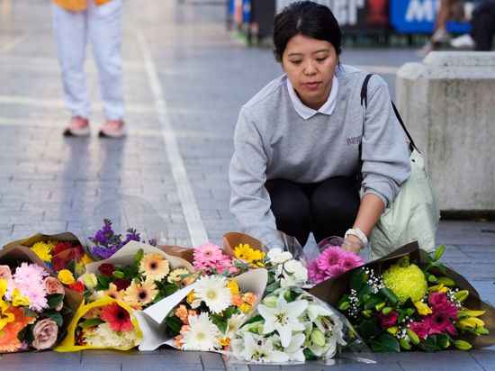 Eine Frau bringt Blumen zu einer improvisierten Gedenkstätte an der Bondi Junction.