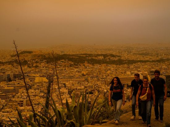 Touristen spazieren auf dem Lycabettus-Hügel, während der Himmel über Athen mit dem antiken Akropolis-Hügel im Hintergrund infolge von Saharastaub eingetrübt ist.