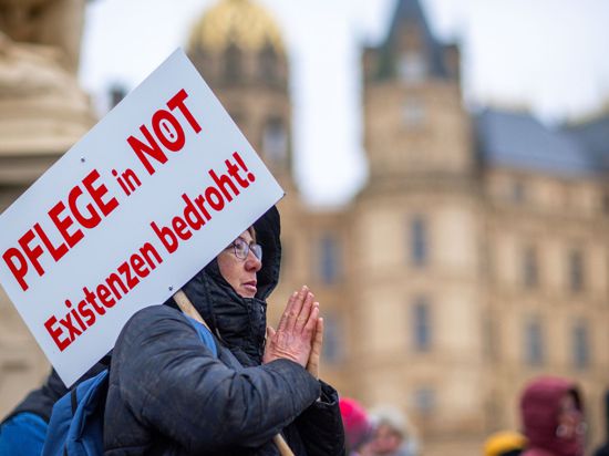 Bei einer Protestaktion vor dem Schweriner Landtag hält eine Teilnehmerin ein Schild mit der Aufschrift „Pflege in Not – Existenzen bedroht!“.