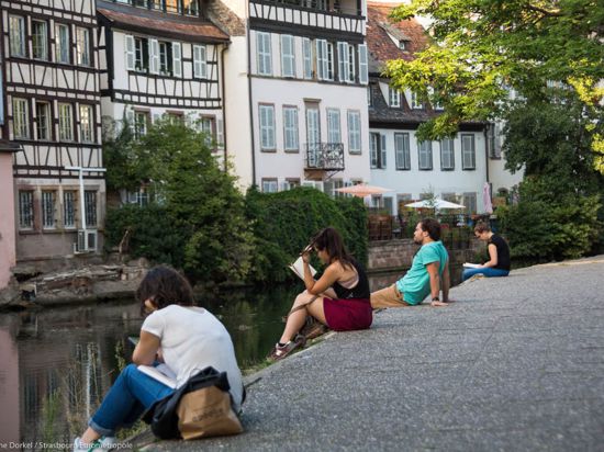 Menschen sitzen an einem Kanal in Straßburg und lesen in Büchern.