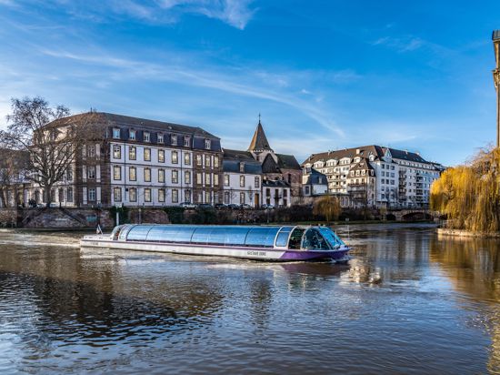 Gebäude, davor fährt ein Boot auf einem Fluss