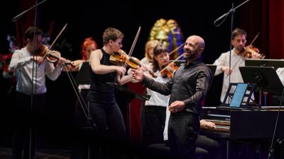 Max Emanuel Cencic singt mit lächelnder Mine im Badischen Staatstheater, während links im Vordergrund die Orchesterleiterin Martyna Pastuszka das Spiel des Orkiestra Historycza leitet. 