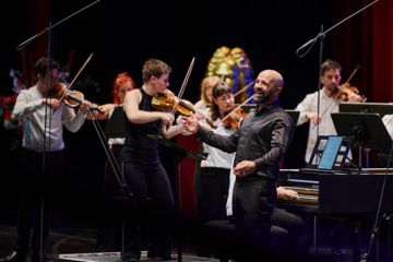 Max Emanuel Cencic singt mit lächelnder Mine im Badischen Staatstheater, während links im Vordergrund die Orchesterleiterin Martyna Pastuszka das Spiel des Orkiestra Historycza leitet. 
