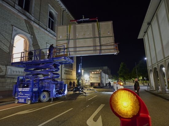 Ein Kran hebt ein großes verpacktes Kunstwerk über eine Straße  in der Nacht
