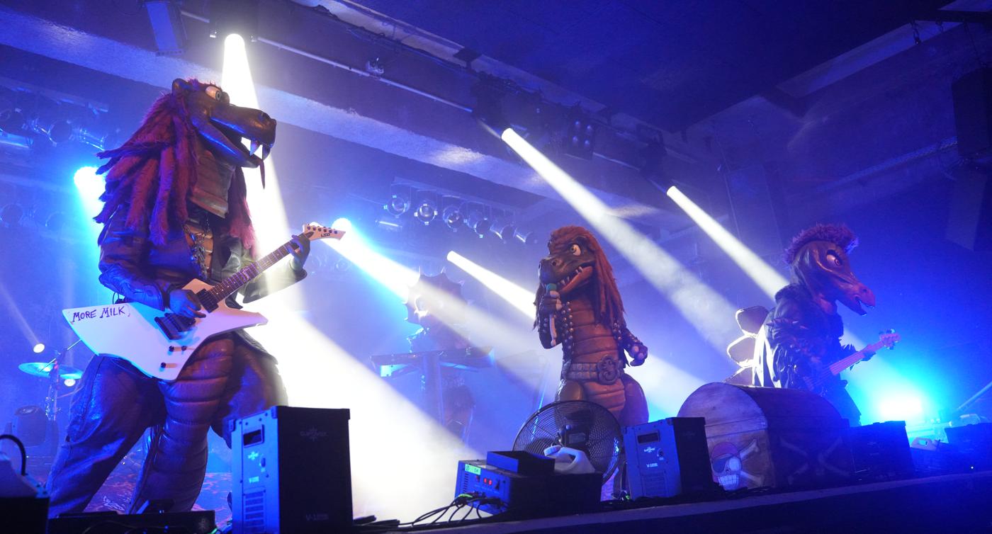 Musiker verkleidet als Dinosaurier auf einer Konzertbühne 