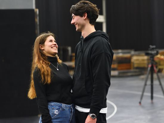 Eine junge Frau und ein junger Mann blicken sich verliebt in die Augen und lachen herzlich während einer Probe in der Nancyhalle Karlsruhe. 