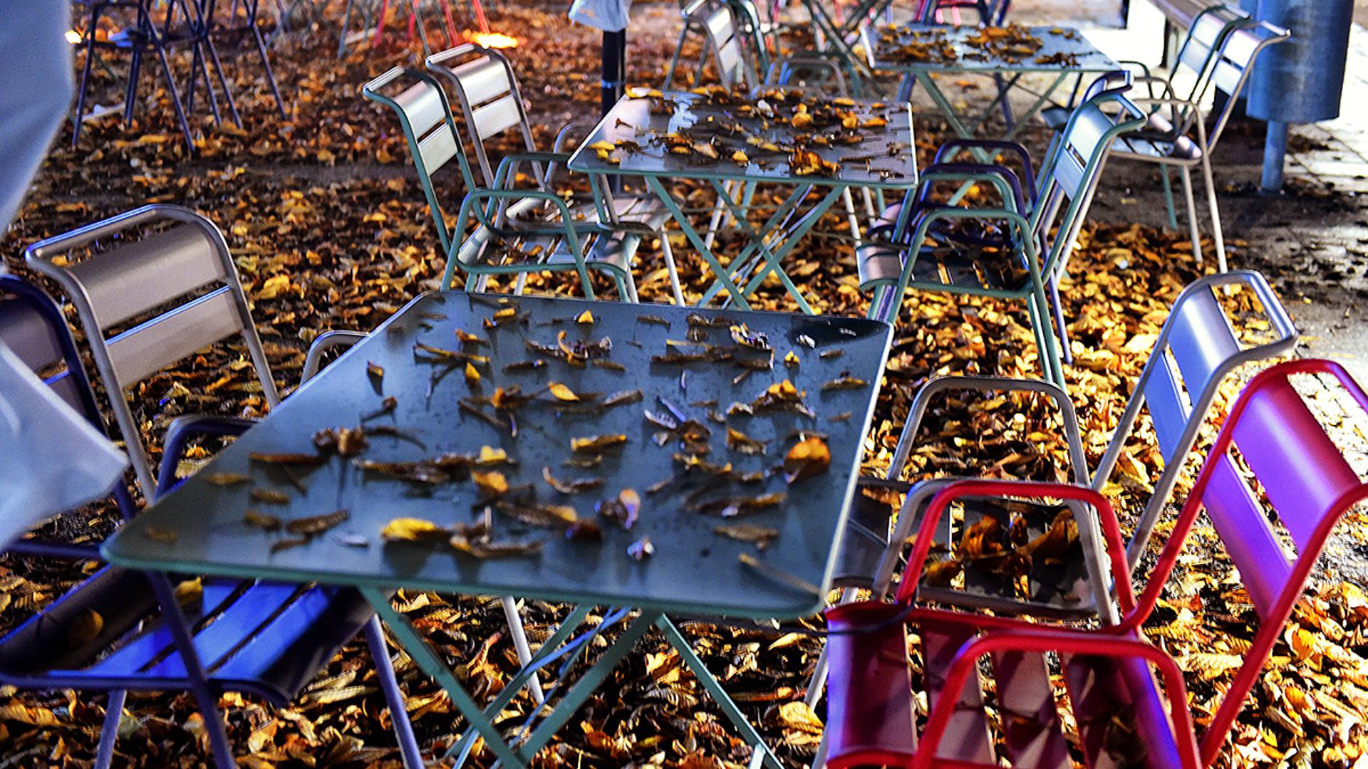 Laub bedeckt Stühle und Tische. Herbst. (Symbolbild).