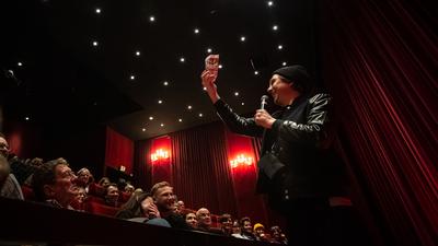 Lars Eidinger hält eine Popcorn-Tüte aus dem Publikum im Karlsruher Kino Schauburg hoch.  
