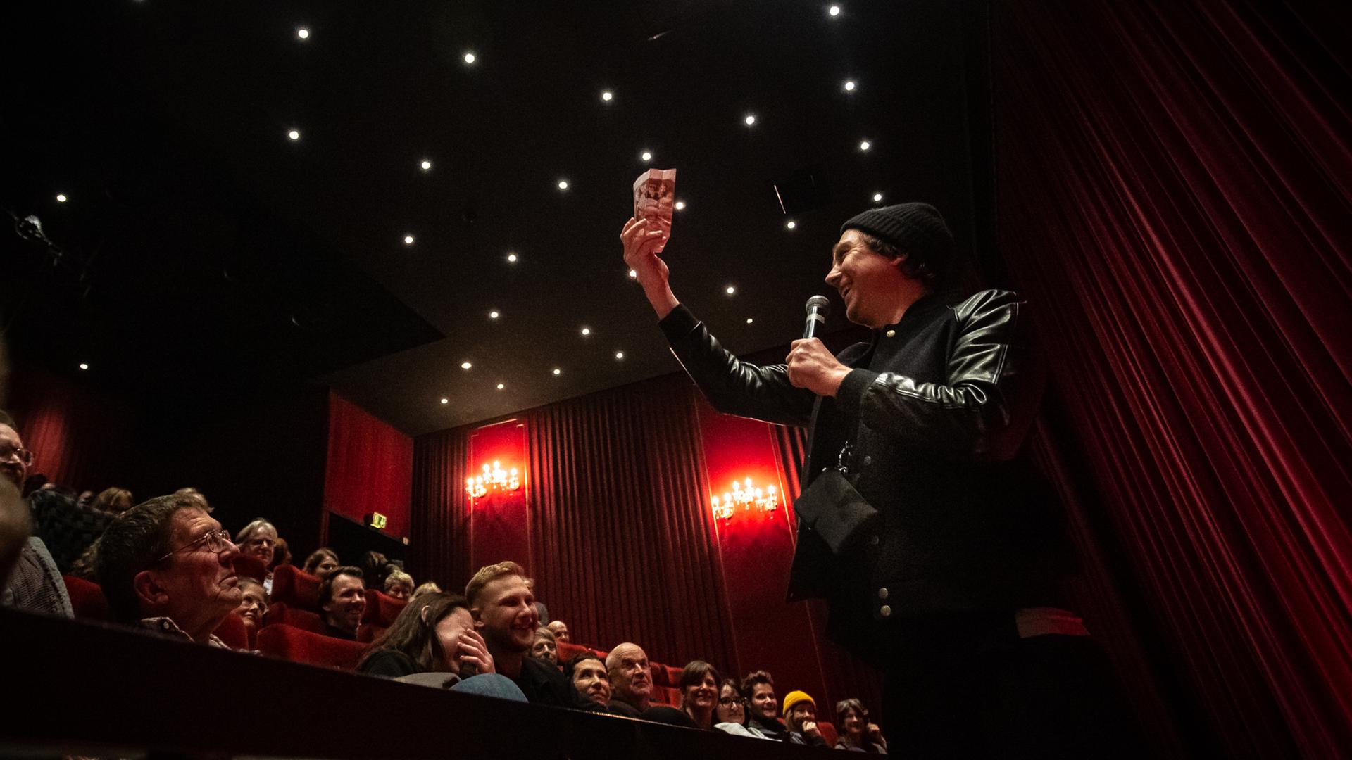 Lars Eidinger hält eine Popcorn-Tüte aus dem Publikum im Karlsruher Kino Schauburg hoch.  