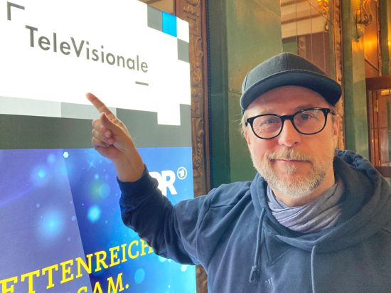 Schauspieler Bjarne Mädel steht im Kurhaus vor einem Monitor mit der Aufschrift „Televisionale“. 