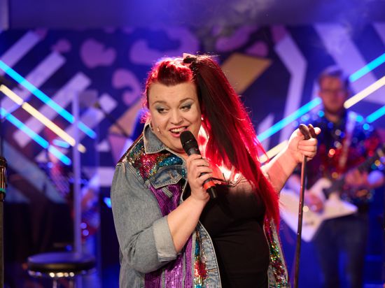 Eine Frau mit roten Haaren steht auf einer Bühne und singt in ein Mikrofon.