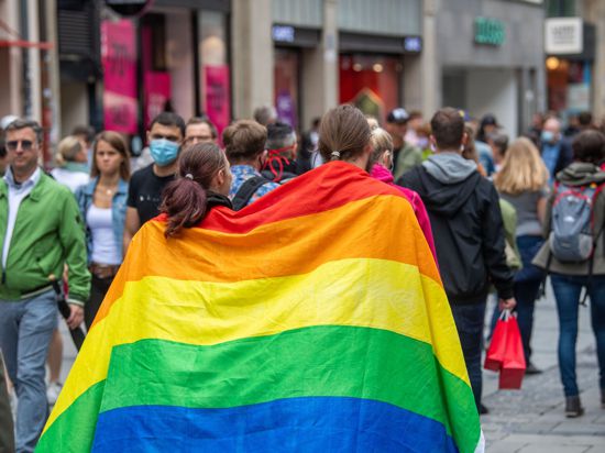 Zwei Frauen laufen umhüllt von einer Pride-Flagge durch die Münchner Innenstadt.