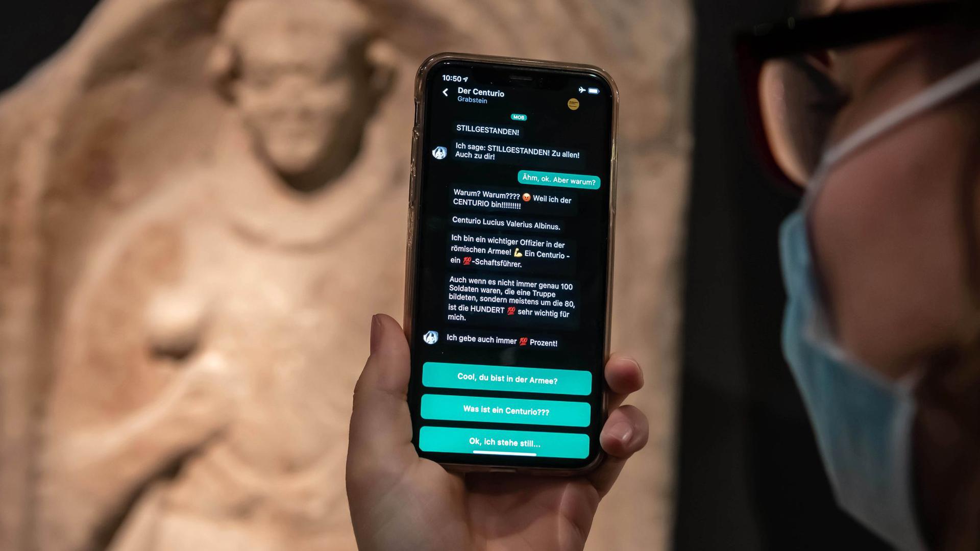 Im Badischen Landesmuseum wird vor einem Grabstein eines Centurio aus dem 1. Jahrhundert nach Christus auf einem Smartphone eine App gezeigt, mit der Museumsbesucher Kontakt zu Ausstellungsobjekten aufbauen können.
