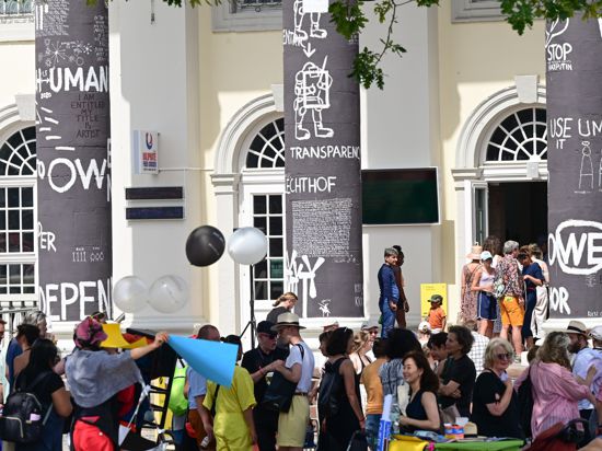 Besucher der documenta fifteen stehen nach Eröffnung vor dem Fridericianum, dessen Säulen der rumänische Künstler Dan Perjovschi mit schwarzer Farbe bemalt und mit weißen Symbolen und Zeichen zu Themen wie Frieden, Solidarität oder Nachhaltigkeit beschriftet hat.