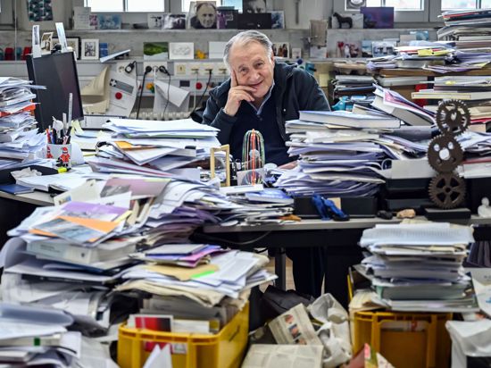 Peter Weibel, Künstler und Direktor des Zentrum für Kunst und Medien (ZKM), sitzt in seinem Büro zwischen aufgetürmtem Papierstapeln.