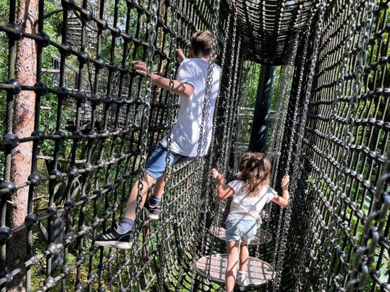 Zwei Kinder gehen und klettern durch den Netztunnel des Baumwipfelpfads beim Biosphärenhaus Fischbach.