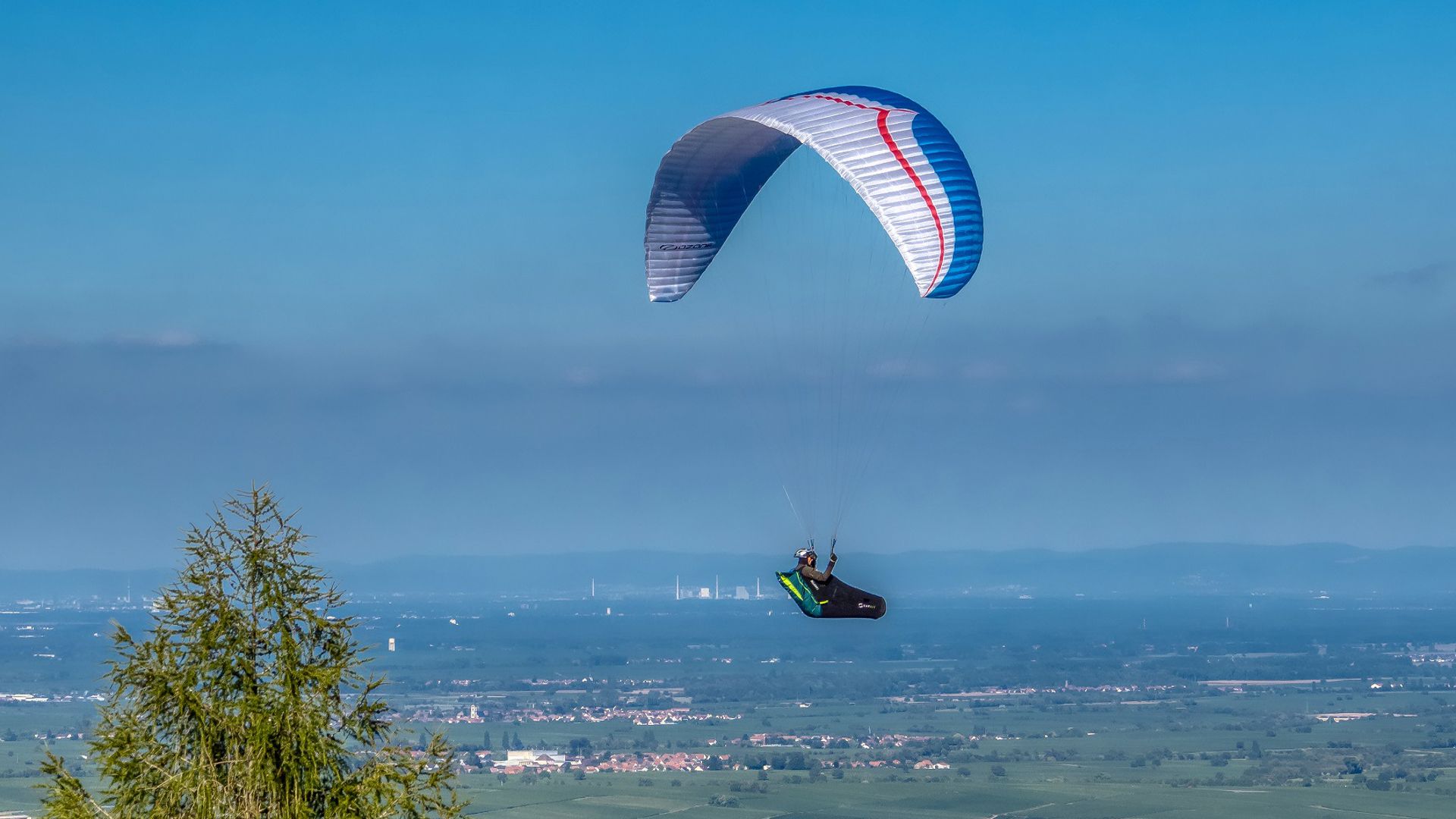 Ein „Pälzer Duddefliecher“, wie Gleitschirmflieger in der Pfalz genannt werden, schwebt hoch über dem Queichtal.