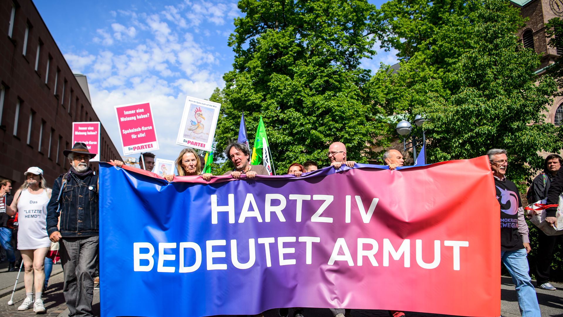 28.04.2018, Baden-Württemberg, Karlsruhe: Demonstranten tragen ein Banner mit der Aufschrift "Hartz IV bedeutet Armut" vor dem Treffen von Bundesgesundheitsminister Spahn mit der Hartz-IV-Kritikerin Schlensog. Vor dem Treffen haben etwa 100 Menschen demonstriert. Die Teilnehmer forderten mehr Geld und eine bessere Behandlung von Beziehern der Sozialleistung. Foto: Sina Schuldt/dpa ++ +++ dpa-Bildfunk +++