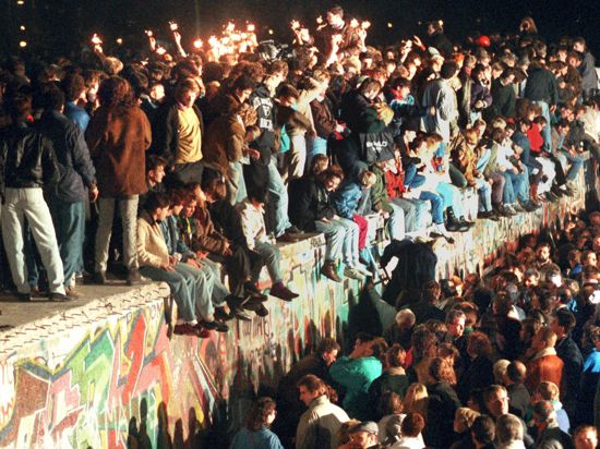 11.11.1989, Berlin: Jubelnde Menschen sitzen mit Wunderkerzen auf der Berliner Mauer. Viele von ihnen fassten später in Westdeutschland Fuß.