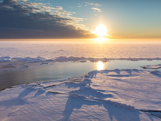 Arktisches Meereis bei Sonnenaufgang. Blick auf einen Schmelzwasserteich und eine Presseiskante im vorderen Bereich.