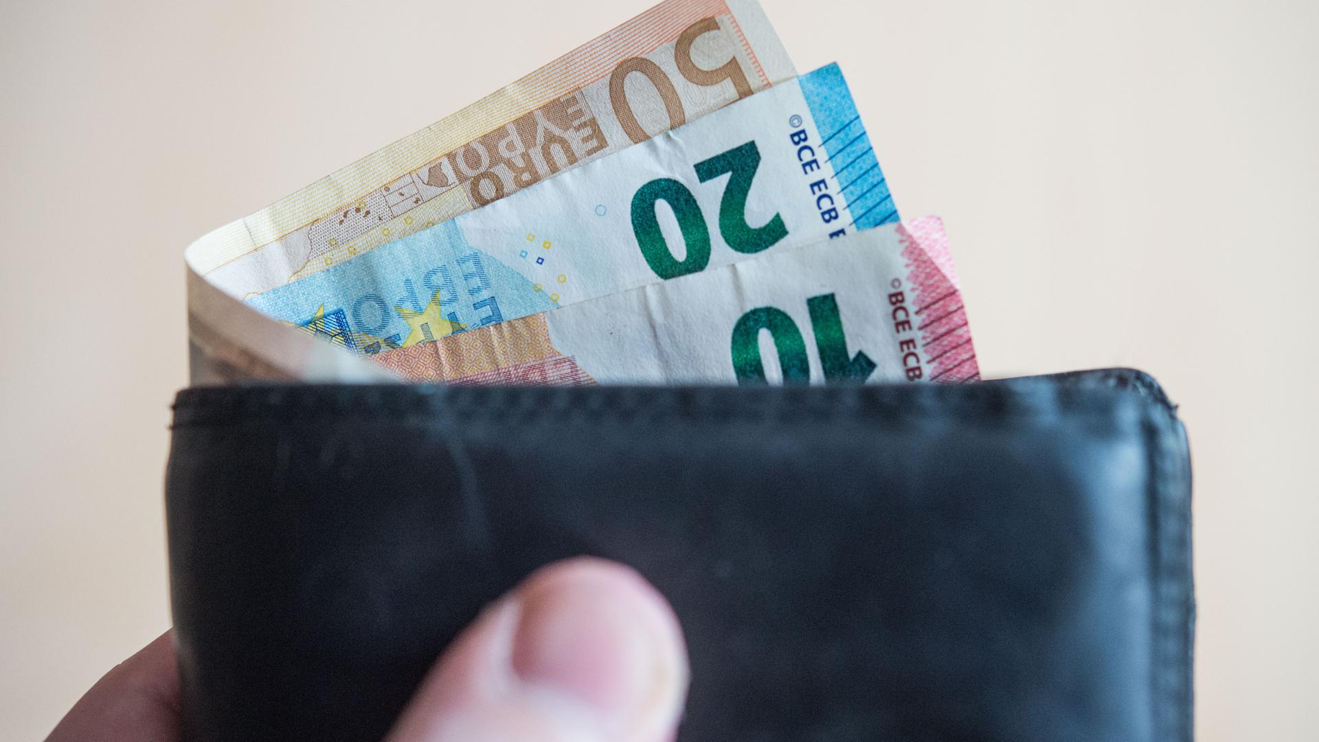 Geldscheine im Wert von zehn, zwanzig, und fünfzig Euro stecken in einem Geldbeutel, der von einer Hand gehalten wird. 