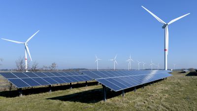 Windkraftanlagen stehen hinter einer Solarstrom-Freiflächenanlage. 