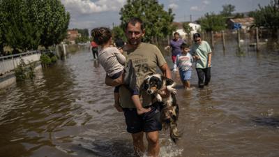 Ein Mann trägt ein Mädchen und einen Hund durch das überschwemmte griechische Dorf Palamas. 