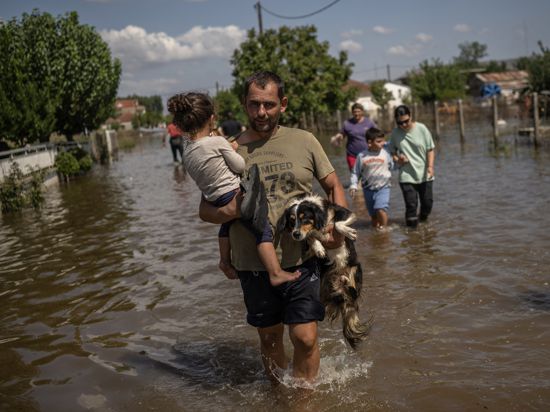 Ein Mann trägt ein Mädchen und einen Hund durch das überschwemmte griechische Dorf Palamas. 