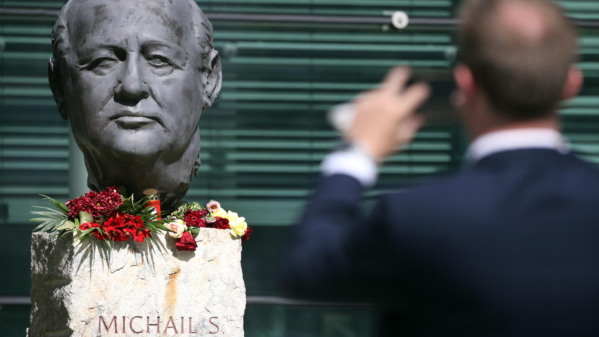 Ein Mann dokumentiert mit seinem Mobiltelefon vor dem Axel-Springer-Verlagsgebäude in Berlin eine Büste von Michael Gorbatschow, an der Unbekannte Blumen niedergelegt haben.