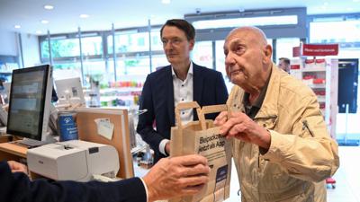 Peter Jordan (86) kauft Medikamente in einer Apotheke, daneben steht Bundesgesundheitsminister Karl Lauterbach. der das neue Verfahren zur Ausstellung eines elektronischen Rezepts vorstellt.