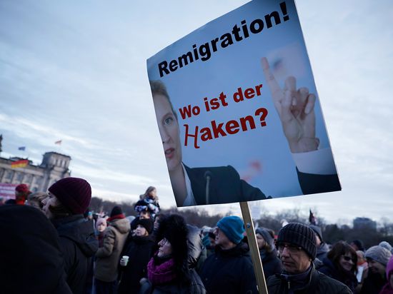 Demonstranten nehmen an einer Protestveranstaltung gegen Rechtsextremismus unter dem Motto “Demokratie verteidigen” vor dem Reichstagsgebäude teil. Zu lesen ist ein Schild mit der Aufschrift "Remigration ! Wo ist der Haken?". Und das H sieht aus wie ein Hakenkreuz.